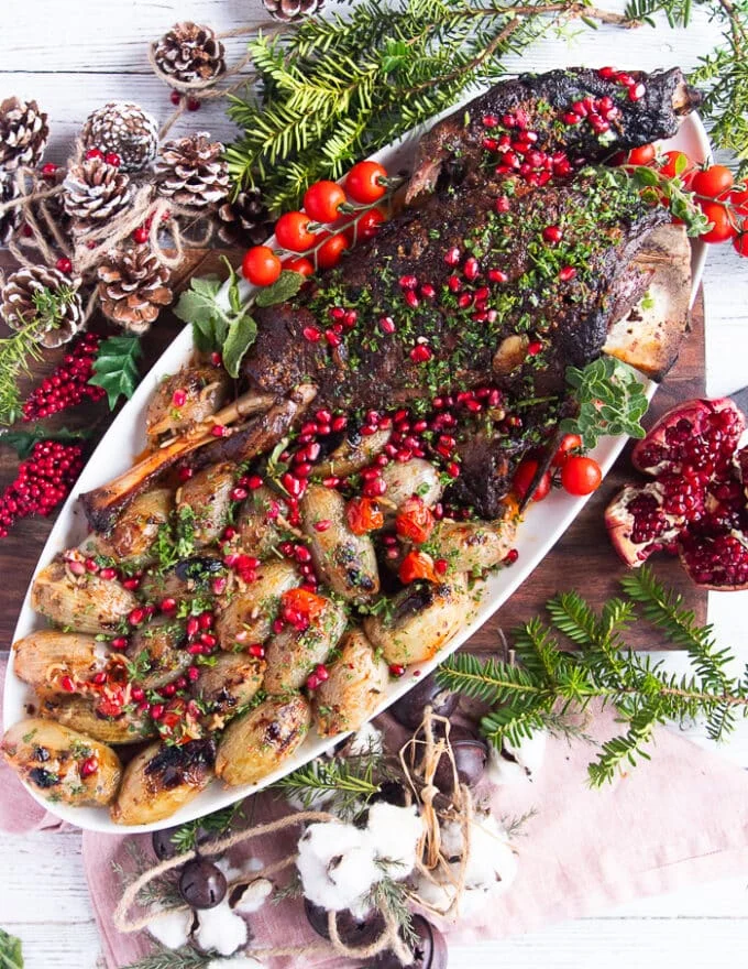 Holiday plate of lamb shoulder roast with stuffed onions around it and some holiday decorations on the table