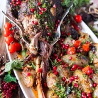 A fork flaking out the tender lamb shoulder roast showing how soft it is on a plate with some stuffed onions