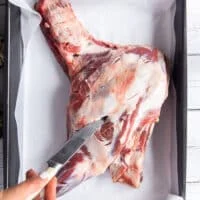 A hand making slits along the lamb shoulder using a small knife