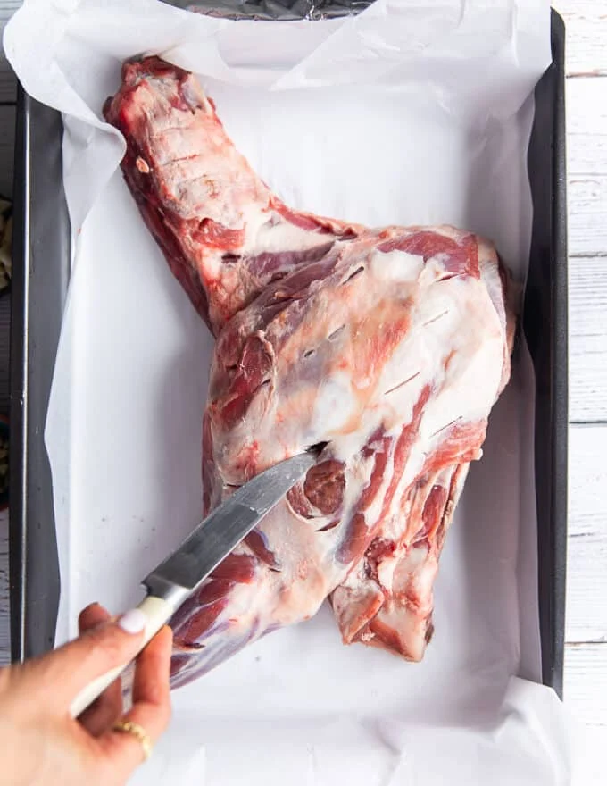 A hand making slits along the lamb shoulder using a small knife