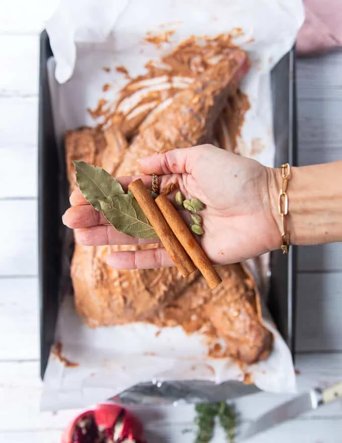 A hand holding whole spices like cinnamon sticks, bay leaves and cardamom pods