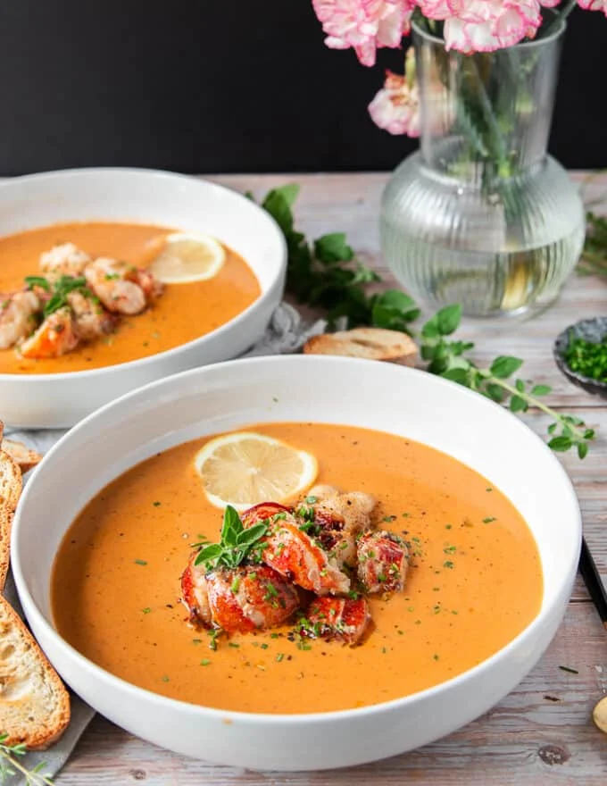 close up of a bowl of lobster bisque, topped with succulent lobster and fresh herbs