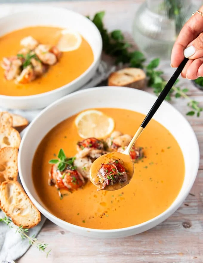 A hand holding a spoonful of lobster bisque close up to the camera showing succulent lobster in a creamy bisque