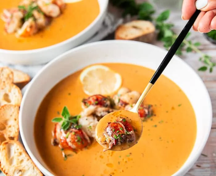A hand holding a spoonful of lobster bisque close up to the camera showing succulent lobster in a creamy bisque
