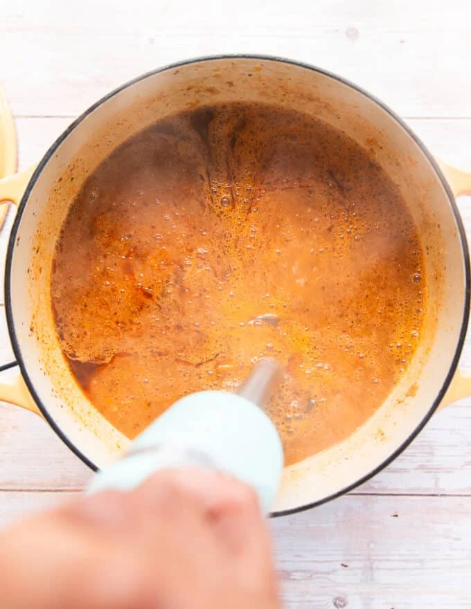 A hand using an immersion blender to blend the smooth into a silky smooth bisque