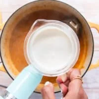 Some cream in a cup being poured into the pot of lobster bisque for a silky creamy finish