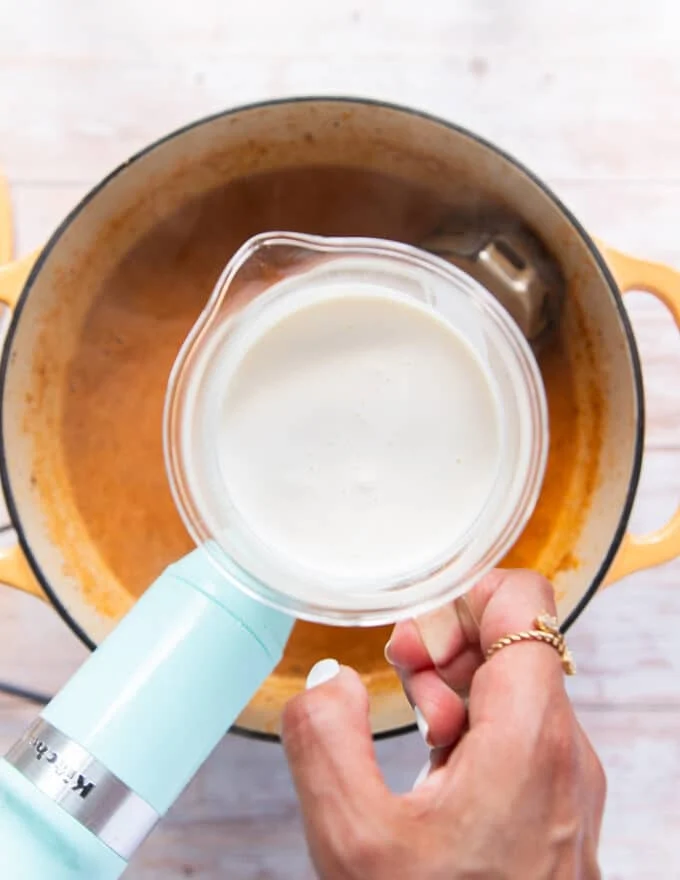 Some cream in a cup being poured into the pot of lobster bisque for a silky creamy finish