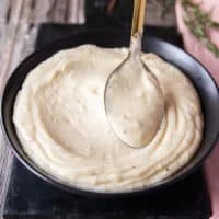 A large spoon smoothing out the surface of the mashed potatoes on a serving plate