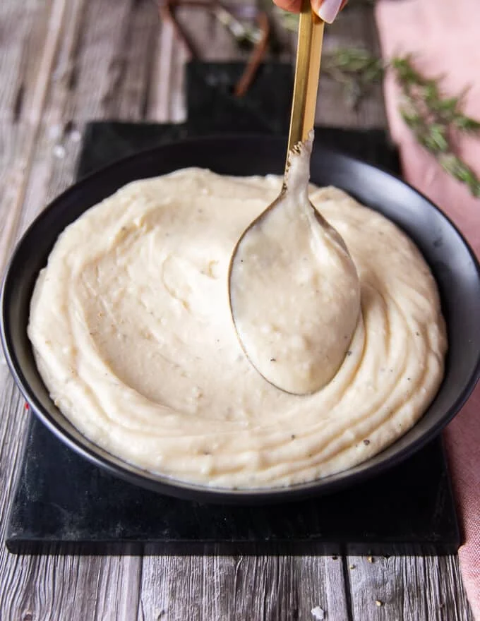 A large spoon smoothing out the surface of the mashed potatoes on a serving plate