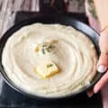 A hand holding a plate of mashed potatoes close up showing a dab of butter melting on the top and a rich creamy spread up mashed potatoes on a plate
