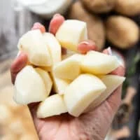 A hand holding peeled and cut up potatoes to about 1 inch thick chunks.