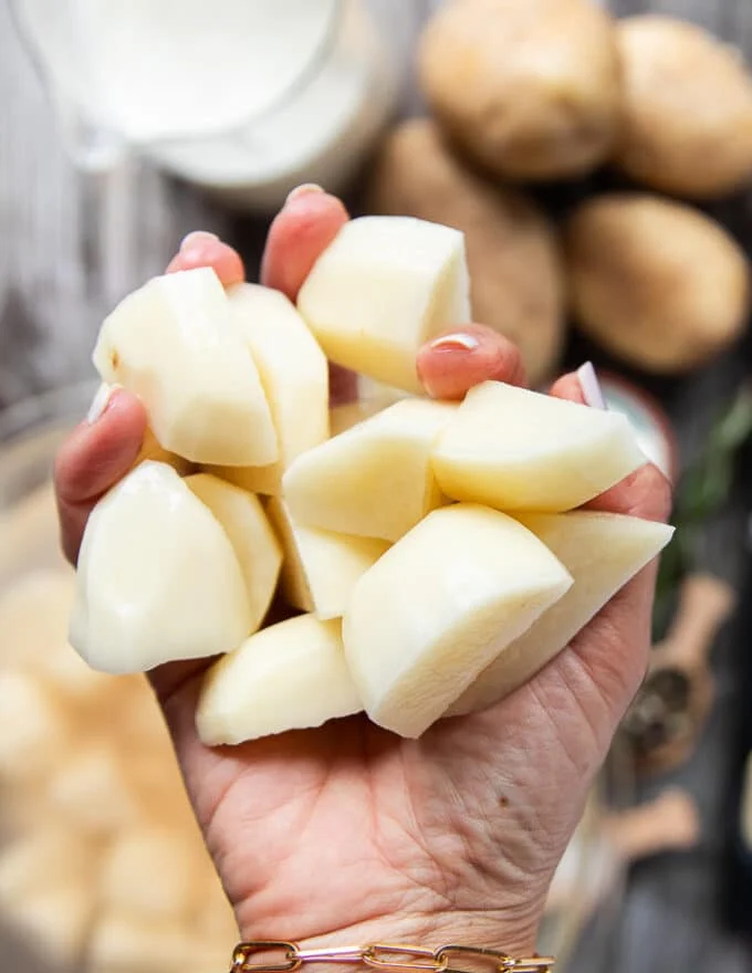 A hand holding peeled and cut up potatoes to about 1 inch thick chunks.