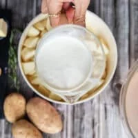 A hand holding a jar of milk and cream mixed together ready to boil in the potatoes with for a creamier mashed potatoes recipes