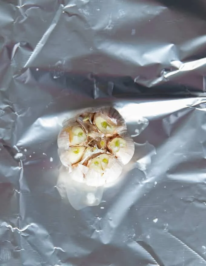 a head of garlic with the tops cut off in the middle of some foil. Drizzled with olive oil and sea salt