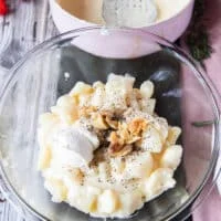 a large bowl with the boiled potatoes, the roasted garlic cloves on top, some butter, seasoning and some cream cheese