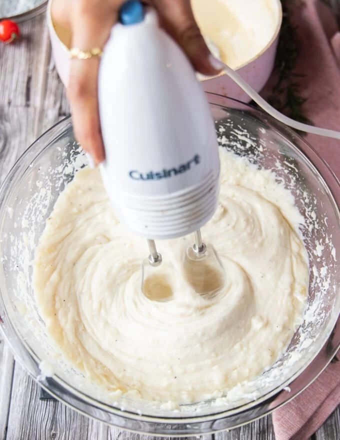 A hand holding a hand mixer and using it to fluff up the potatoes and mash them instead of a potato masher