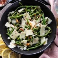 close up of a plate of perfectly sautéed green beans garnished with parmesan shavings, some lemon zest, chilli flakes and toasted nuts