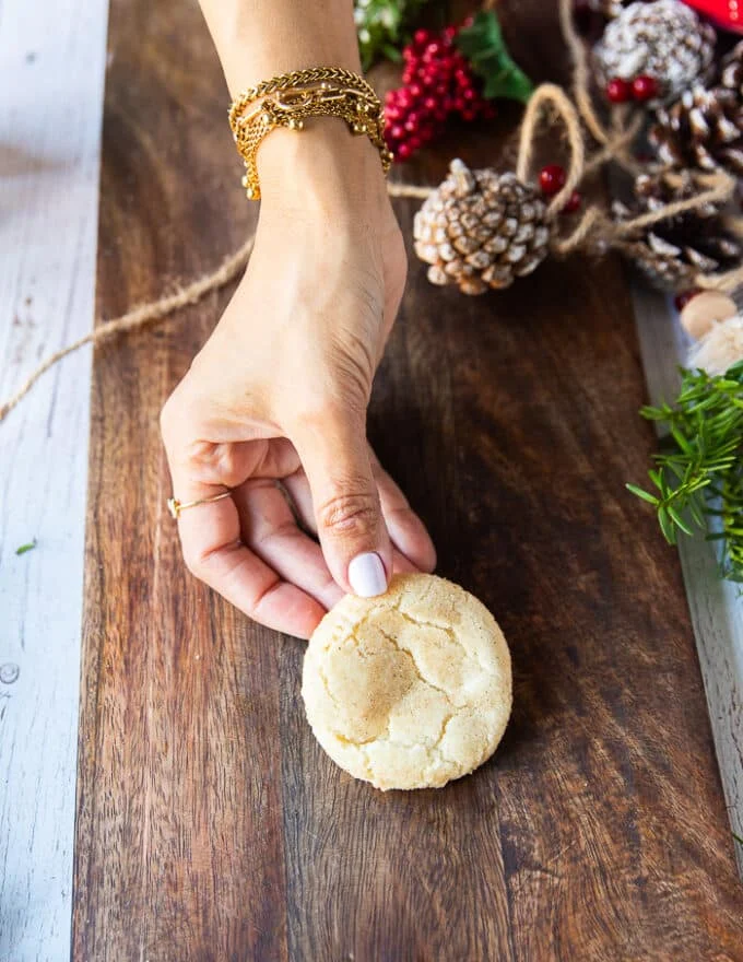 A hand holding one perfectly baked sugar cookie on a board showing the texture of it close up