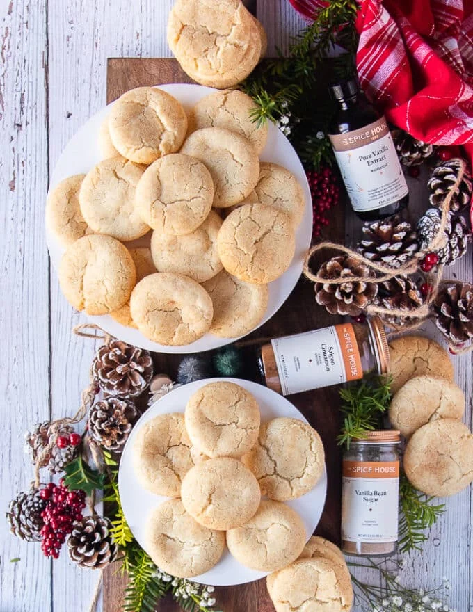 Two plates of sugar cookies right out of the oven served alongside pine cones and holiday ribbons