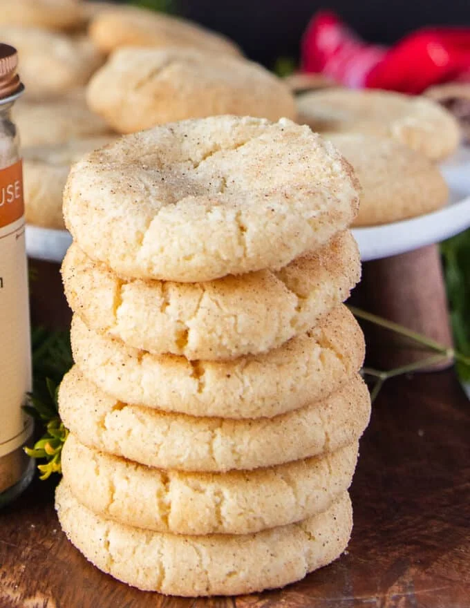 Long stack of 6 sugar cookies on top of each other showing the texture and specs of vanilla bean on a wooden board