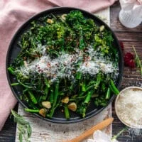 A plate of broccoli rabe perfectly sautéed and garnished with parmesan cheese and chilli flakes