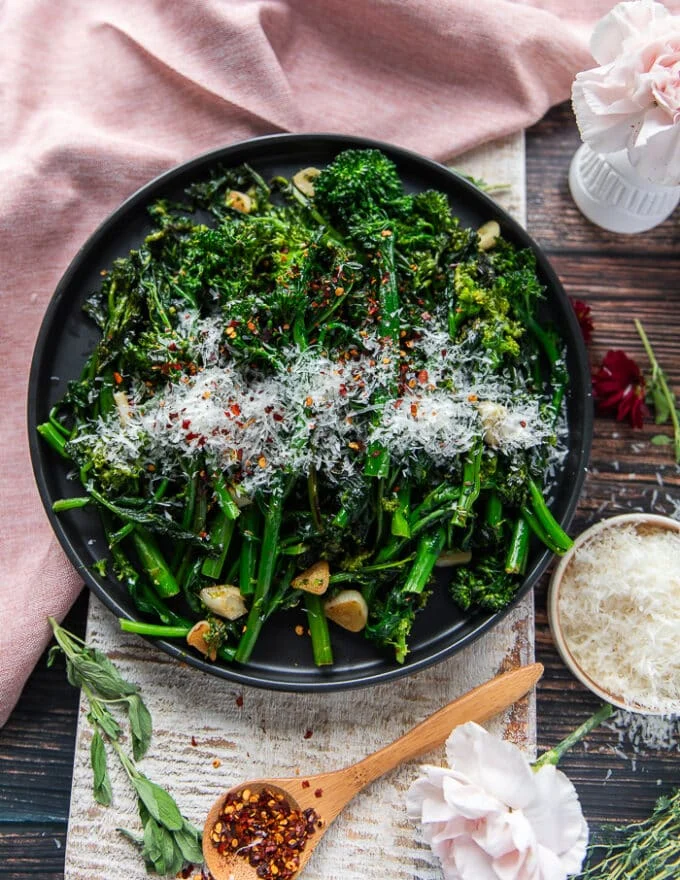 A plate of broccoli rabe perfectly sautéed and garnished with parmesan cheese and chilli flakes