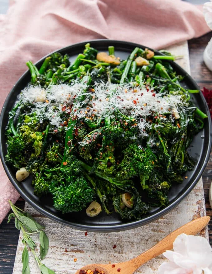 Side view of a plate of cooked rapini with lots of parmesan on top and chilli flakes