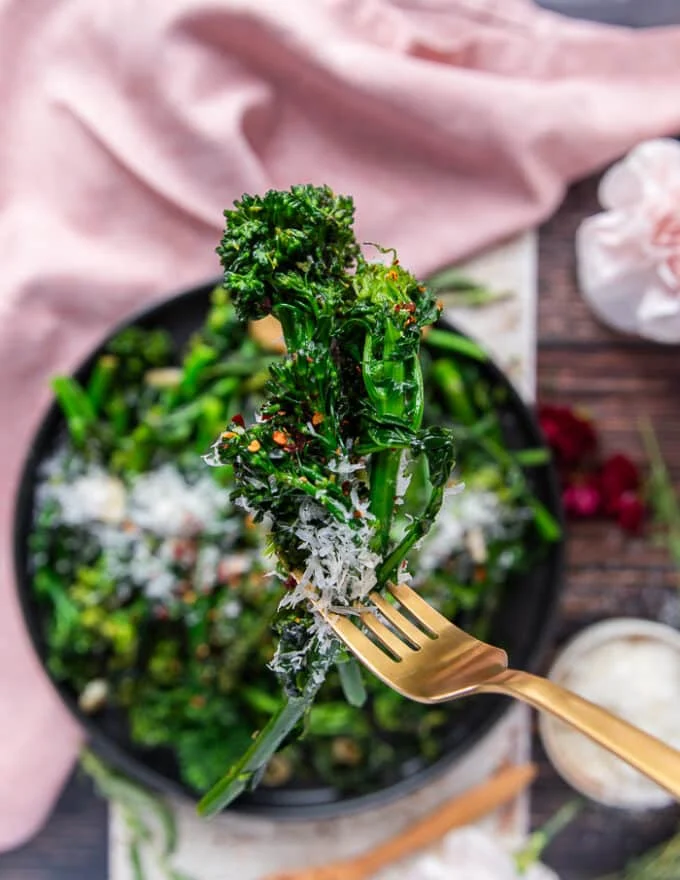 A hand holding a closeup of cooked broccoli rabe showing the perfect green color, and soft texture with a sprinkle of chilli flakes and parmesan cheese