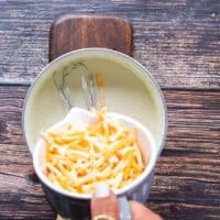 The cheese is being added into the pot to make the sauce cheesy