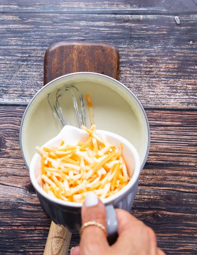 The cheese is being added into the pot to make the sauce cheesy
