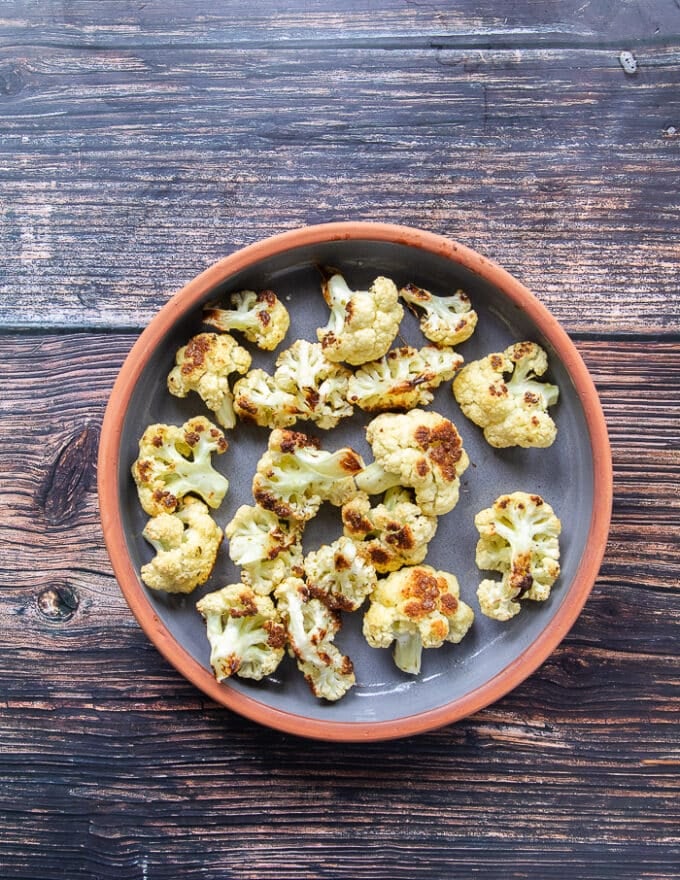 The roasted cauliflower is spread at the bottom of an oven safe casserole dish