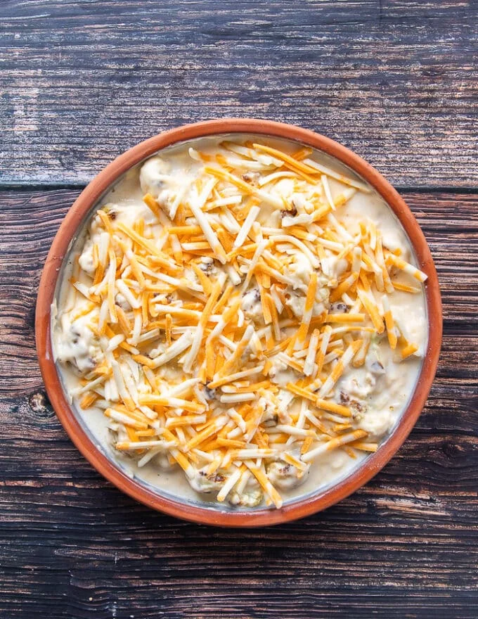 A layer of cheese is spread over the cauliflower and sauce in the casserole right before baking. The casserole is now ready to bake
