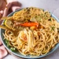 A hand holding a fork and showing close up some crab tossed in pasta with a lemon garlic zesty sauce