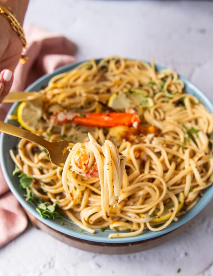 A hand holding a fork and showing close up some crab tossed in pasta with a lemon garlic zesty sauce