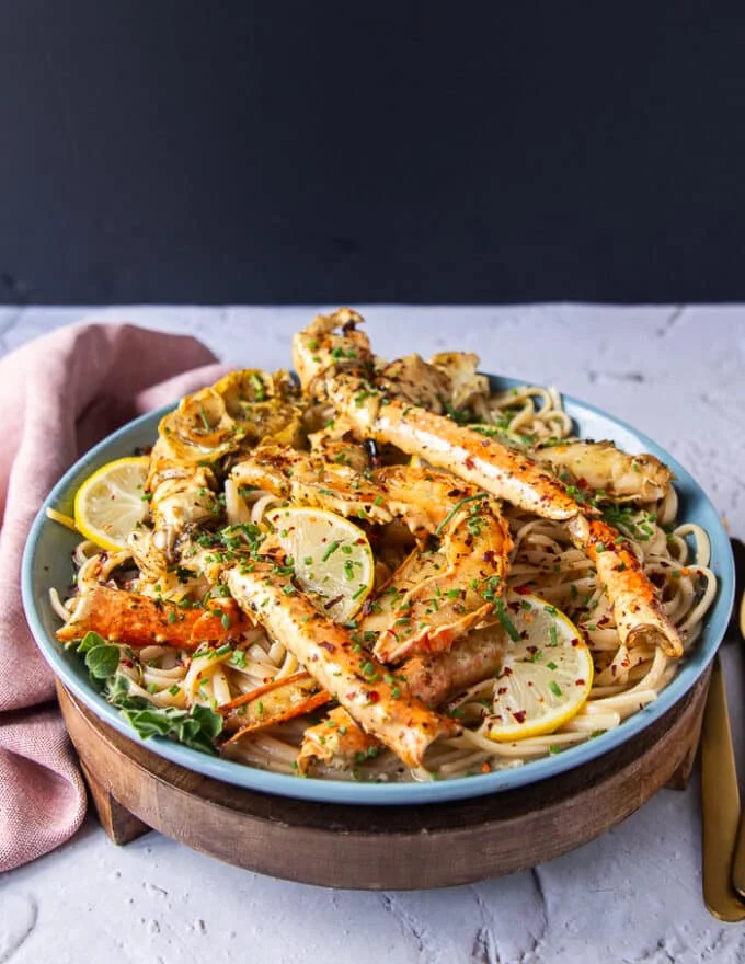 A plate of the cooked crab pasta with the crab on top and more herbs, some lemon slices and chilli flakes