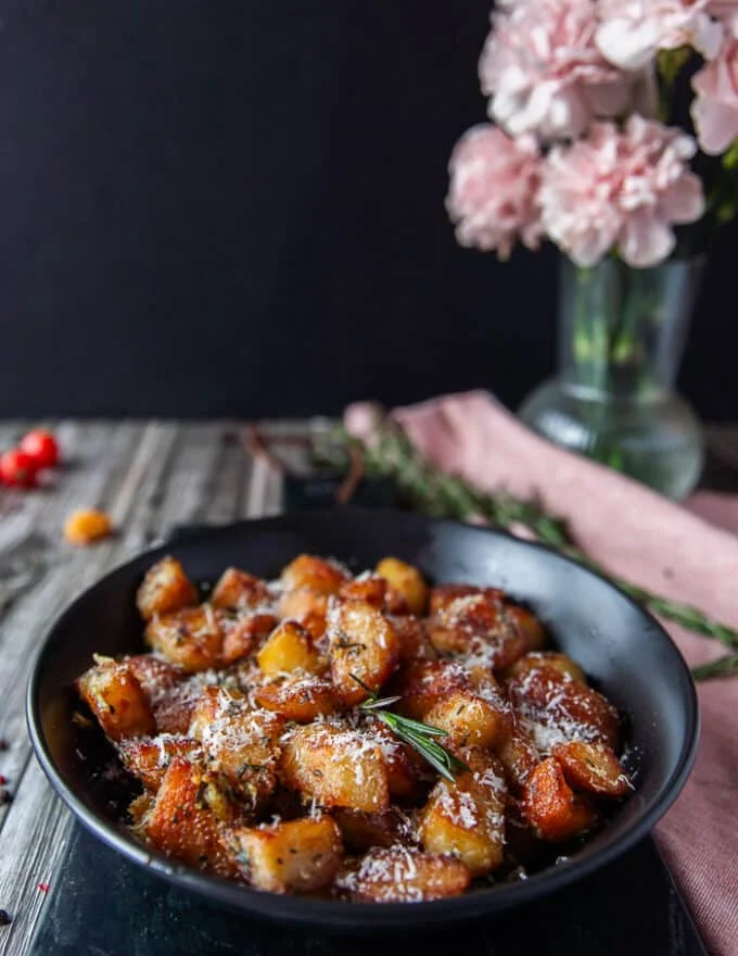 crispy potatoes on a plate sprinkled with extra parmesan cheese, and fresh rosemary sprigs served and ready