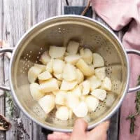 A hand holding a colander with the boiled potatoes drained and ready