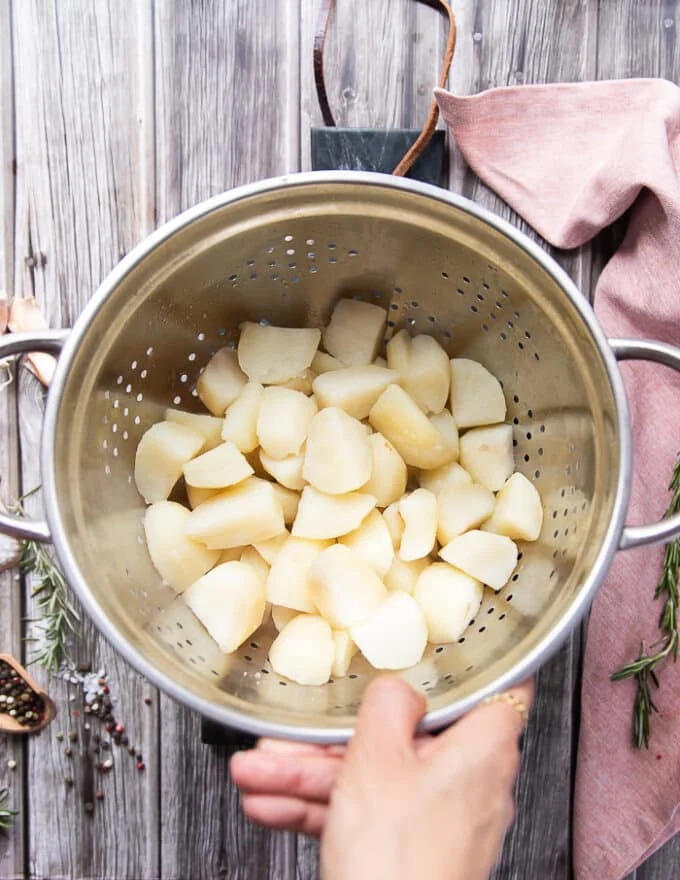 A hand holding a colander with the boiled potatoes drained and ready