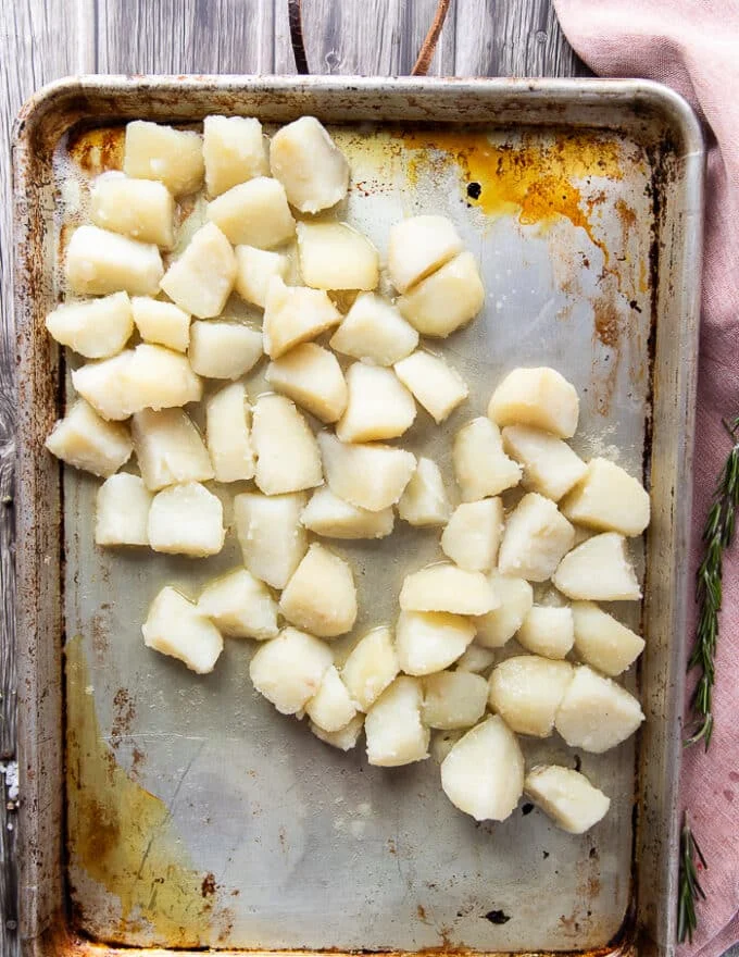 The drained potatoes added into the hot baking sheet with hot oil