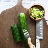 A hand using a fork to scorch the cucumbers for them to absorb maximum dressing