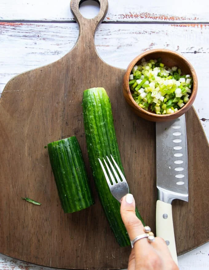 A hand using a fork to scorch the cucumbers for them to absorb maximum dressing