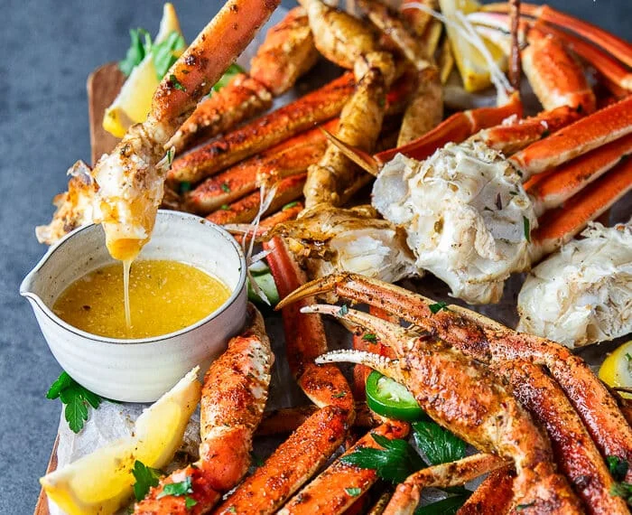 A hand dipping a cooked crab leg into a bowl of melted butter and the butter dripping from it close up