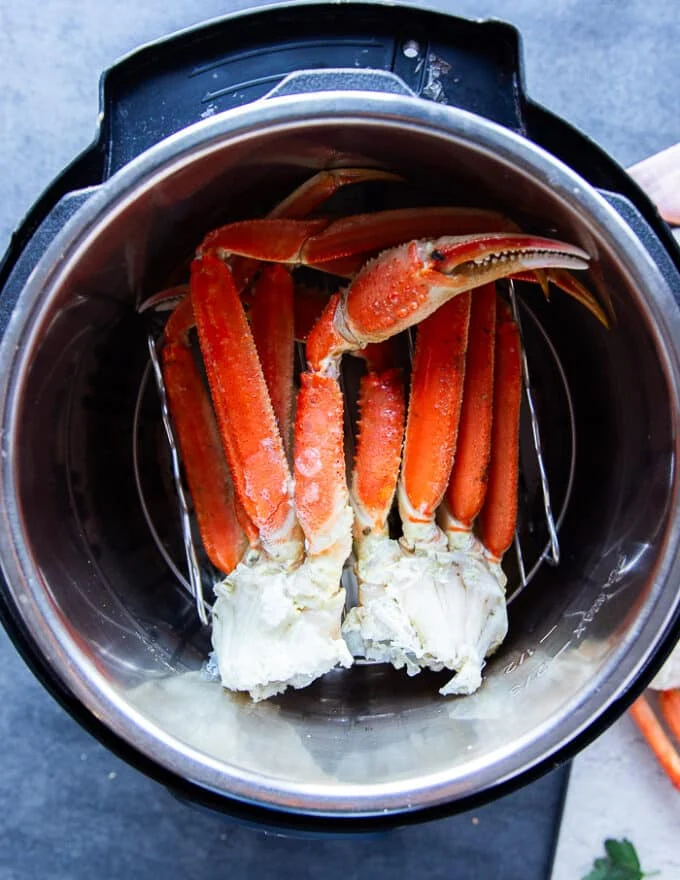 A set of crab legs placed in an instant pot steamer with lemon, bay leaf and garlic at the water for steaming