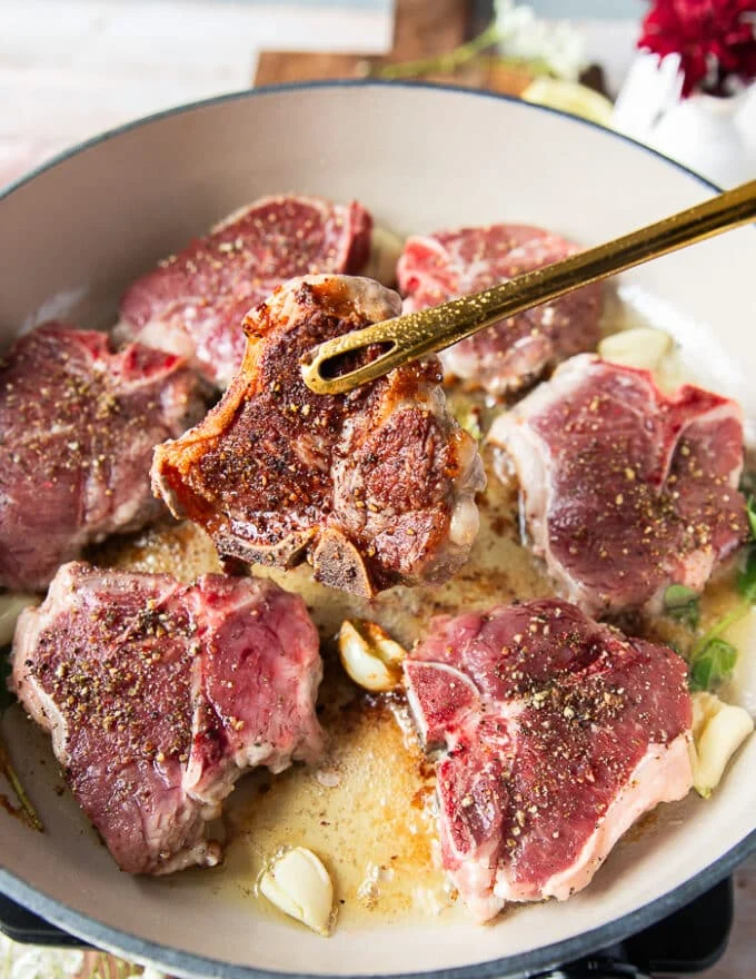 A tong holding one piece of lamb chop and flipping it over to show the perfect browning
