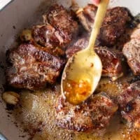 A spoon basting some butter from the skillet over the lamb chops to infuse them and cook them