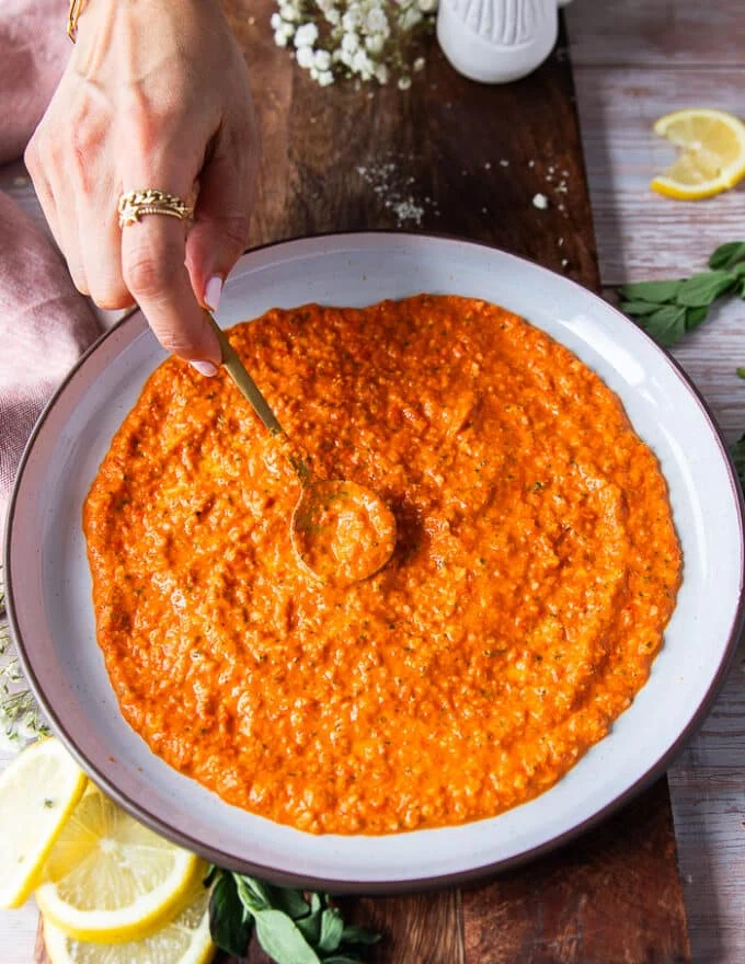 A hand spreading a layer of romesco sauce over the plate