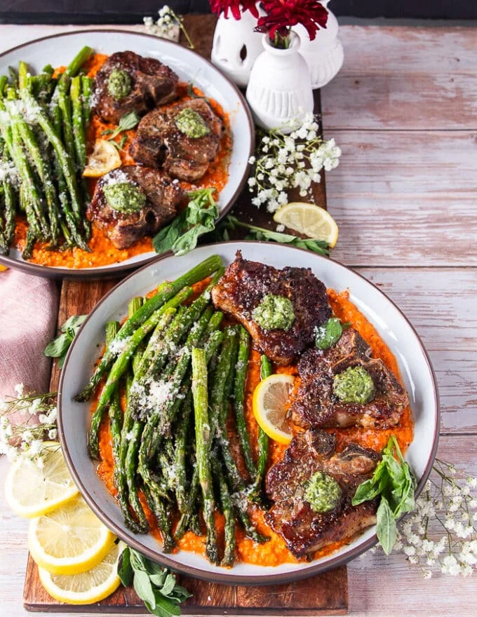 two plates of plated lamb chops with air fryer asparagus over romesco sauce