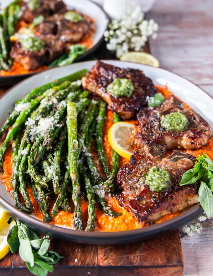 close up of the plated lamb chops showing how well cooked and buttery they are with dollops of basil pesto on top