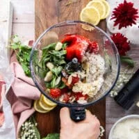 A food processor with all the romesco sauce ingredients added in one go including roasted red peppers, cherry tomatoes, almonds, lemon juice, fresh basil, olive oil, garlic, parmesan cheese and lemon juice