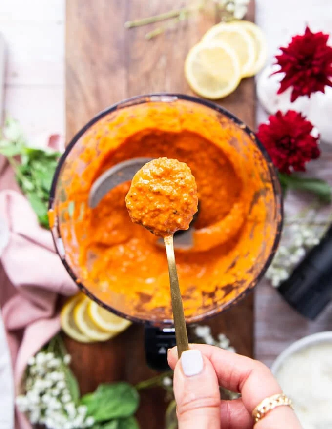 A spoon showing close up the texture of the romesco sauce when processed shwoing the vibrant orange color and how slightly chunky it is